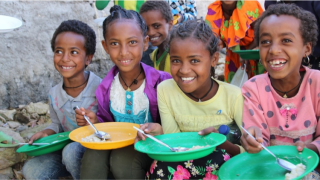 Children in Ethiopia smiling eating a plate of Mary's Meals