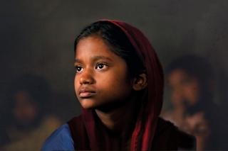 Child wearing red headscarf against a dark backdrop