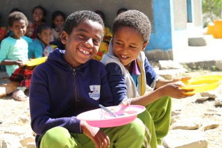 Two boys sitting outside eating bowls of Mary's Meals in Ethiopia