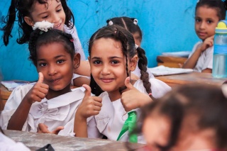 Two school children give thumbs up to camera in school