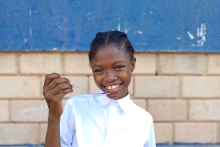 Girl smiles while holding bowl and cutlery outside school in Liberia