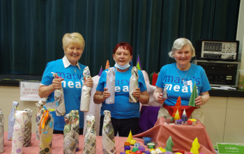 Three members of Blairgowrie volunteer group at a stall with crafts in Mary's Meals blue t-shirts