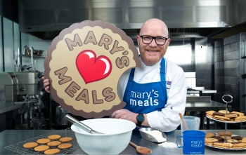 Chef Gary Maclean with Mary's Meals blue apron on and biscuit prop