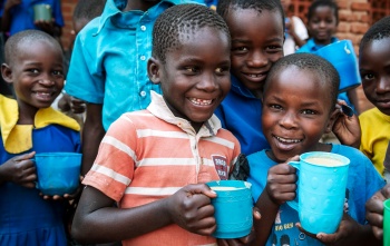 Young children holding blue Mary's Meals porridge mugs and smiling for camera