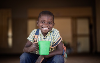 Smiling child holding mug of Mary's Meals porridge