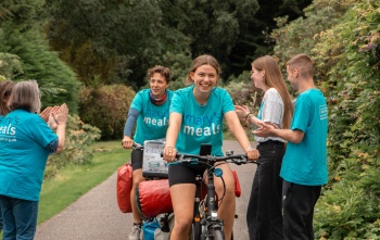 Jacob and Lucia cycling and being cheered on by supporters