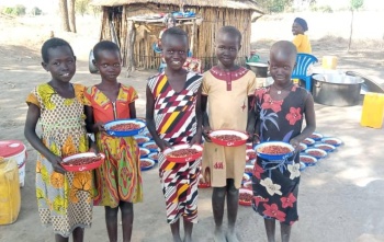 Smiling school children holding plates of maize and beans