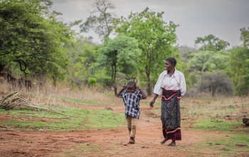 Mother and young son walk through bush in rural Zambia together