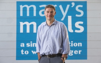 Founder of Mary's Meals, Magnus MacFarlane-Barrow (man) standing in front of Mary's Meals logo