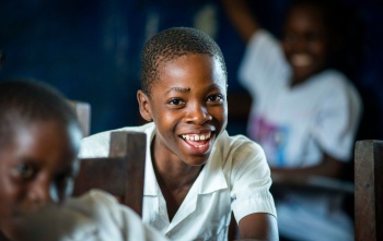 A boy sits in a classroom, smiling