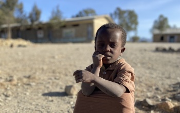 A child in Ethiopia sits on the dusty ground.