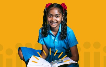 Girl smiling at camera with open book in lap against yellow background
