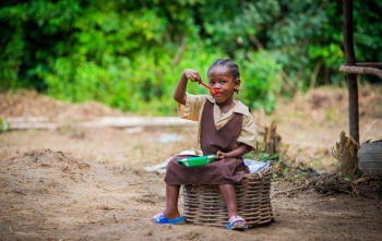A girl sitting outside eating Mary's Meals in Liberia