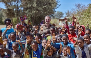 Magnus MacFarlane-Barrow standing alongside a group of happy school children in Ethiopia