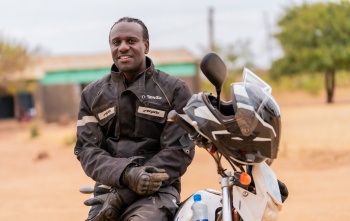 Amos Lungu, a school feeding officer from Zambia, sits on a motorbike