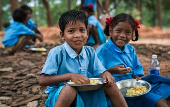 Two children sit together eating Mary's Meals