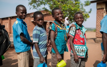 Four boys outside in Malawi standing with mugs