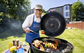Gary Maclean holds a piece of meat over a BBQ with food cooking