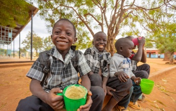Boys in Zambia sit outside with mugs of Mary's Meals