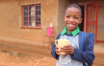 Image of a child holding their food outside of a school in Malawi