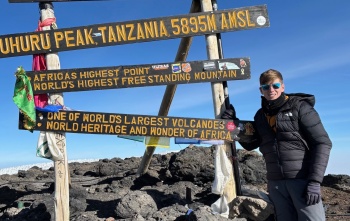 Teenager Lochlan stands at a sign signalling that he is at the summit of Mount Kililmanjaro