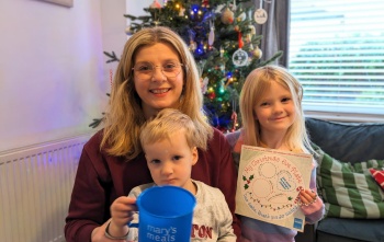 Victoria and her children in a living room, a boy holds a Mary's Meals mug and a girl holds a Santa plate