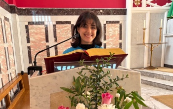 A woman, Alessandra, stands behind a pulpit in a church