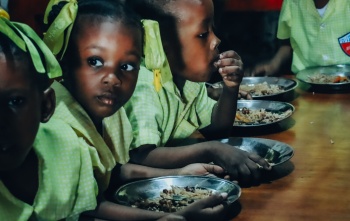Children in Haiti eating meals at a long table