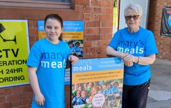 A woman and a girl stand in Mary's Meals t-shirts next to a Mary's Meals sign