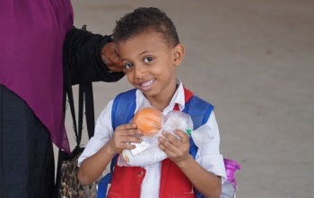 A young boy stands holding an orange