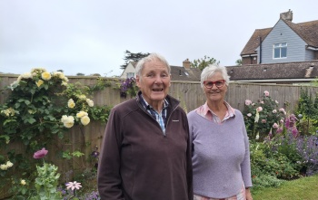 An elderly couple stand in a garden together