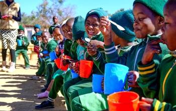 Children eating from mugs outside