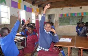 Kids in a classroom with their hands up