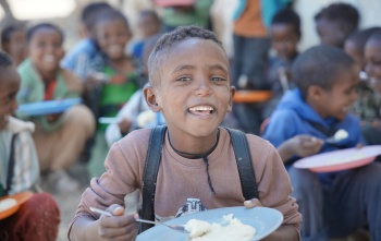 A happy boy eating a bowl of food