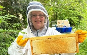 A woman in a beekeeping outfit holding honeycomb