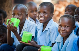 Three Zambian boys in school uniform holding a mug of porridge