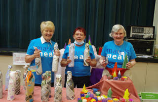 Three members of Blairgowrie volunteer group at a stall with crafts in Mary's Meals blue t-shirts