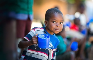 Child in Malawi holding mug of porridge