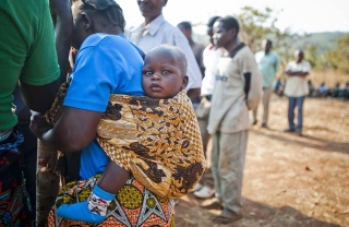 A small baby sitting in a sling on the back of a woman