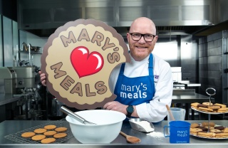 Chef Gary Maclean with Mary's Meals blue apron on and biscuit prop