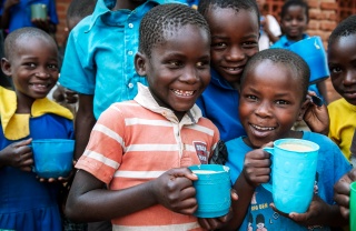 Young children holding blue Mary's Meals porridge mugs and smiling for camera
