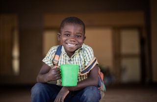 Smiling child holding mug of Mary's Meals porridge