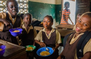 Children eating Mary's Meals and smiling in classroom in Liberia
