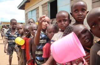 children in Kenya queuing for their lunch, mugs in hand