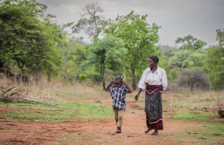 Mother and young son walk through bush in rural Zambia together