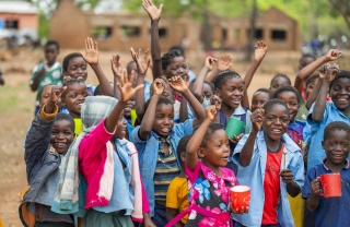 Children in playground at school in rural Zambia raise hands and smile