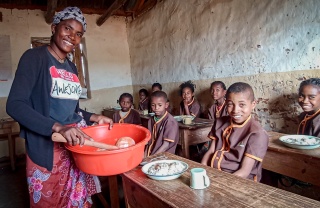 A volunteer cook serves food to children in a classroom