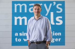 Founder of Mary's Meals, Magnus MacFarlane-Barrow (man) standing in front of Mary's Meals logo