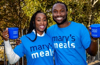 Scarlette and Stuart Douglas standing together smiling holding Mary's Meals mugs and wearing Mary's Meals t-shirts