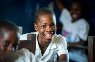 A boy sits in a classroom, smiling